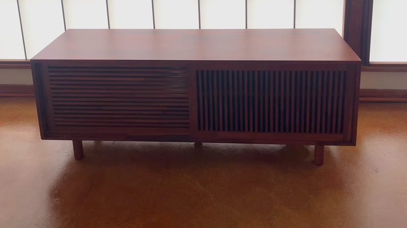 Walnut media console with slatted doors on a wood floor